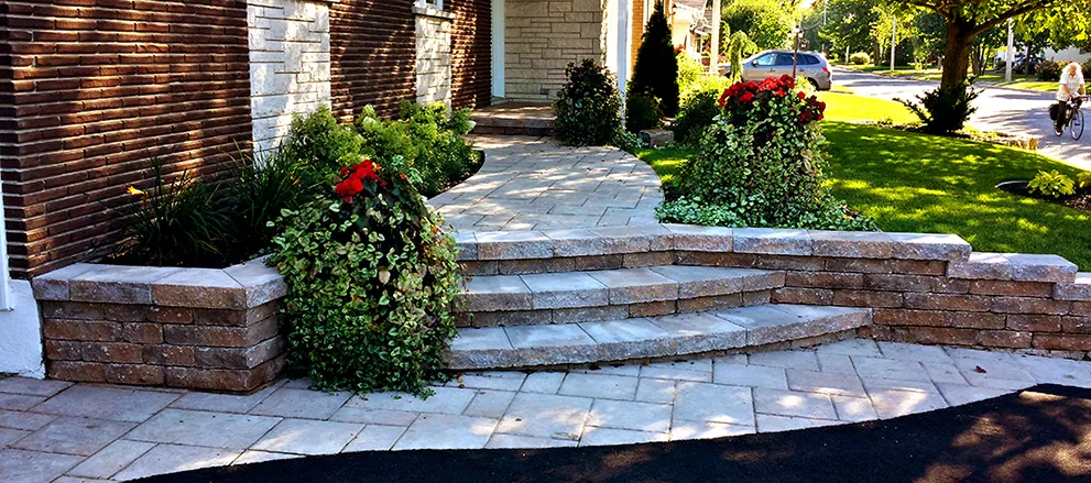 Escalier courbe en blocs et allée de pavé menant à l’entrée d’une maison de brique, entourés de fleurs