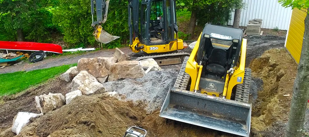 Mini-pelle et chargeuse sur chenilles déplaçant de grosses pierres sur un chantier