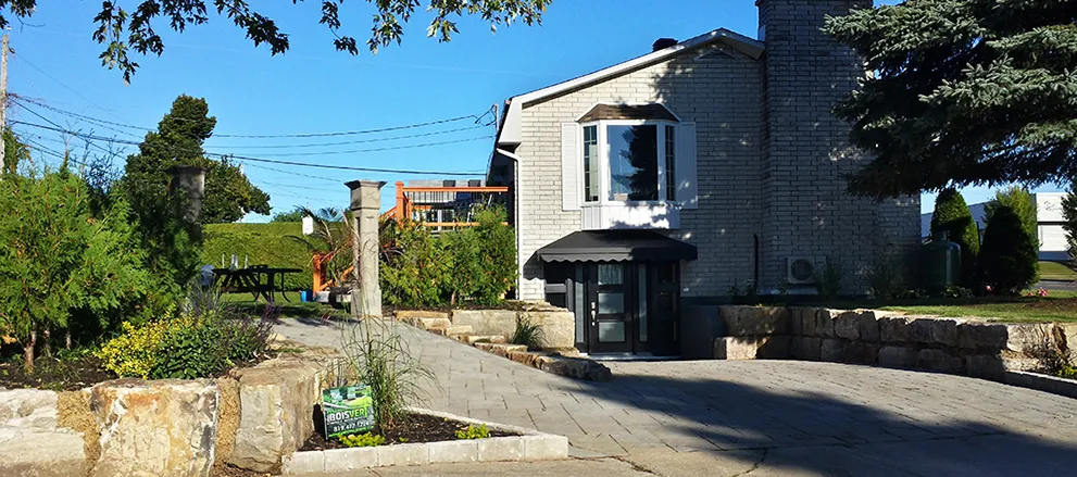 Terrain aménagé avec allée de pavé, murets de pierres et pancarte Aménagement Paul Boisvert devant une maison