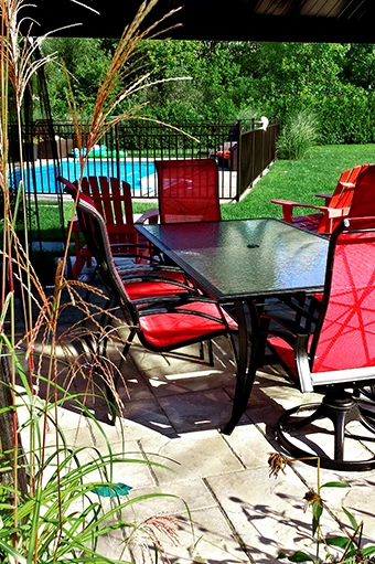 Patio de dalles sous abri avec mobilier rouge, devant une piscine et un terrain gazonné